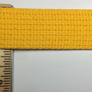 May include: A close-up of a bright yellow woven cotton webbing. The webbing is about 1 inch wide and has a textured surface.