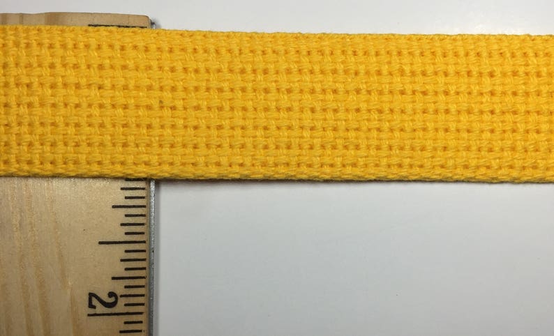 May include: A close-up of a bright yellow woven cotton webbing. The webbing is about 1 inch wide and has a textured surface.