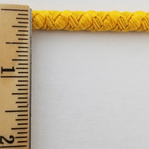 May include: A close-up of a bright yellow braided cord, measured against a ruler. The cord is approximately 1 inch wide.