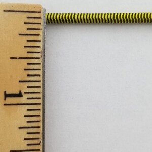 May include: A close-up of a yellow and black striped elastic cord measured against a ruler. The cord is about 1 inch long.