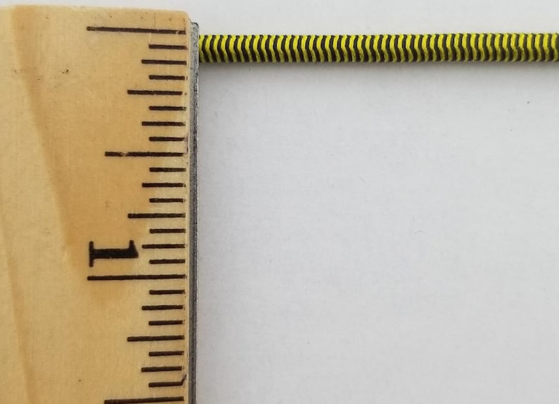 May include: A close-up of a yellow and black striped elastic cord measured against a ruler. The cord is about 1 inch long.
