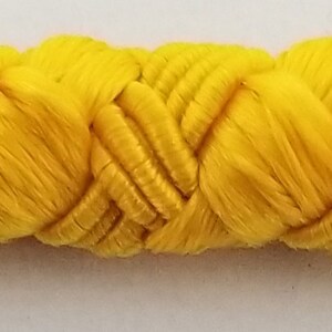May include: A close-up of a yellow braided trim. The trim is made of a soft, woven fabric and has a slightly textured surface.