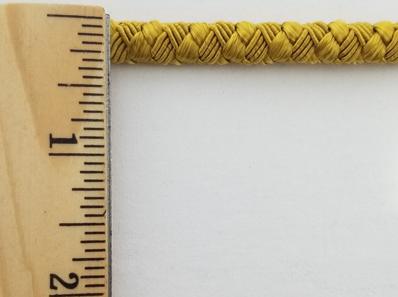 May include: A close-up of a yellow braided cord, measured against a ruler. The cord is approximately 1 inch wide.