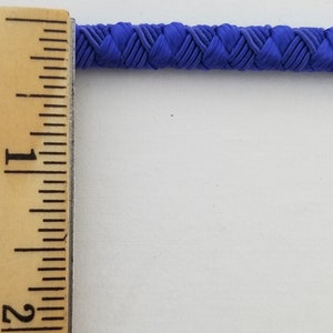 May include: A close-up of a blue braided cord measured against a ruler. The cord is approximately 1 inch wide.