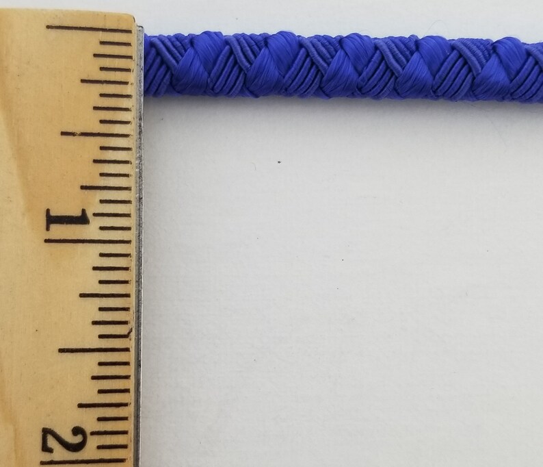 May include: A close-up of a blue braided cord measured against a ruler. The cord is approximately 1 inch wide.