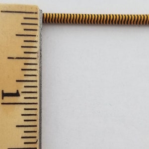 May include: A close-up of a black and yellow striped elastic cord, measured against a wooden ruler with inch markings. The cord is approximately 1 inch long.