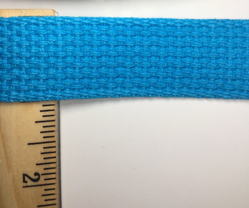 May include: A close-up of a bright turquoise woven cotton webbing, measured against a wooden ruler with the number "2" visible.