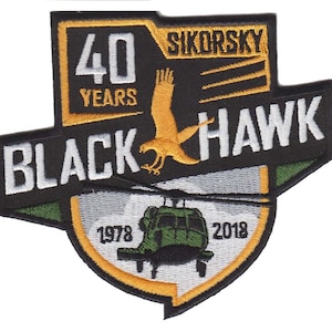 May include: A black and green embroidered patch with a white helicopter, a yellow hawk, and the text "Sikorsky Black Hawk 40 Years 1978-2018".