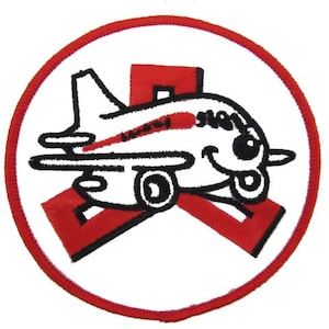 May include: A white airplane with a red stripe and a smiling face is flying over a red X in a red circle.