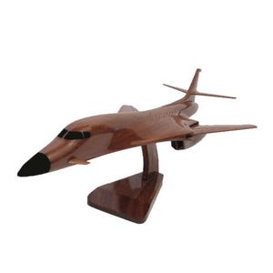 May include: A wooden model of a B-1B Lancer bomber aircraft. The model is painted in a dark brown color and is mounted on a wooden base.