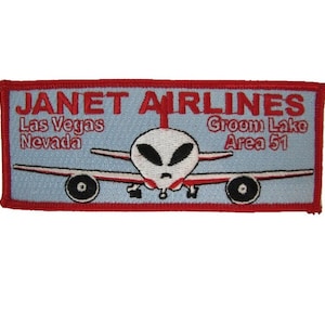 May include: A red, white, and blue embroidered patch with the text "JANET AIRLINES" and the words "Las Vegas Nevada" and "Groom Lake Area 51". The patch features a cartoon airplane with an alien pilot.