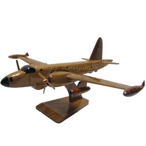 May include: A wooden model of a Lockheed P-3 Orion aircraft. The model is painted in a natural wood finish and has black accents. The model is on a wooden stand.