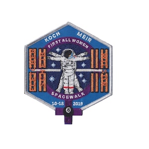 May include: Embroidered patch with a blue, purple, and gold design. The patch features an astronaut in a spacesuit, the text "FIRST ALL WOMEN SPACEWALK", and the names of the astronauts. The date "10-18 2019" is also included.