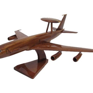 May include: A wooden model of an aircraft with a distinctive radar dome on top. The model is a rich brown color, with detailed wings, engines, and a stand. The aircraft model is a decorative item.