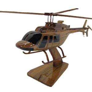 May include: A wooden model helicopter with a glossy finish. The model features a detailed design, including the rotor blades, tail rotor, and windows. The helicopter is mounted on a wooden base. The text "military" is visible on the side of the helicopter.