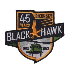 May include: Black Hawk 45 Years patch with a green helicopter, a yellow hawk, and the text "Sikorsky" and "1978 - 2023".