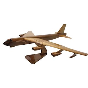 May include: A wooden model of a B-52 Stratofortress bomber airplane. The model is painted in a natural wood finish and is displayed on a wooden stand.