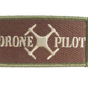 May include: A brown embroidered patch with a green border. The patch features a white drone icon and the text "DRONE PILOT".