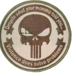 May include: Round patch with a skull design in brown and white, surrounded by text in a circular pattern. The text reads "Despite what your momma told you... Violence does solve problems."