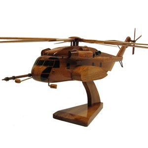 May include: A wooden model of a brown Sikorsky CH-53E Super Stallion helicopter with a detailed interior and a stand. The helicopter has a long, slender fuselage and a large, powerful rotor system.