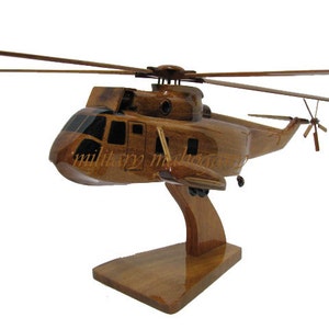 May include: A wooden model of a helicopter, featuring a detailed design with a brown finish. The model includes a main rotor, tail rotor, and is mounted on a wooden stand. The text "military monuments" is visible on the side of the helicopter.
