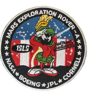 May include: A black and white embroidered patch with a cartoon character saluting. The patch features the text "Mars Exploration Rover - A", "NASA", "Boeing", "JPL", "Cornell", "15LS", and "Red Planet Gladiators".