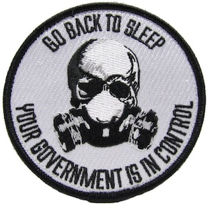 May include: White embroidered patch with a black skull wearing a gas mask. The text reads "Go Back To Sleep Your Government Is In Control."