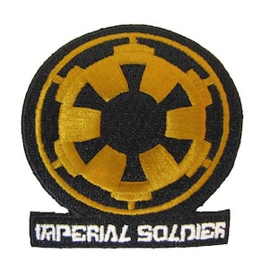 May include: A black and gold embroidered patch with the Imperial symbol from Star Wars. The text "Imperial Soldier" is below the symbol.