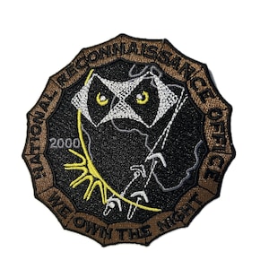 May include: A brown embroidered patch with the text "National Reconnaissance Office" and "We Own The Night" around a black and white image of a bat with the year 2000 in the upper left corner.