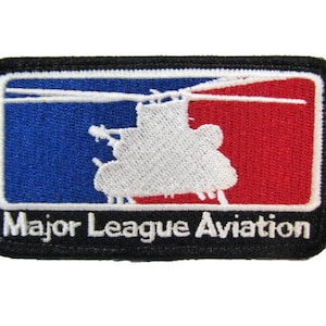 May include: A black and white embroidered patch with a red, white, and blue baseball logo. The logo features a helicopter silhouette. The text "Major League Aviation" is below the logo.