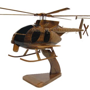 May include: A wooden model of a helicopter with a black and brown paint scheme. The helicopter is on a wooden stand and has a tail rotor.