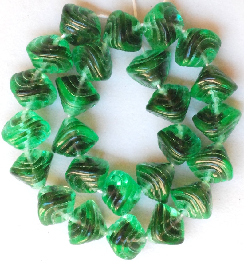 May include: A strand of green glass beads with a swirl design. The beads are faceted and have a translucent appearance.