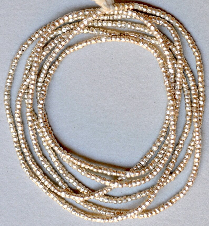 May include: A strand of silver-toned beads, arranged in a circle, on a white background.
