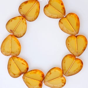 May include: A strand of amber-colored glass heart beads. The beads are strung together with a thin white thread. The beads are all heart-shaped and have a slightly translucent appearance.