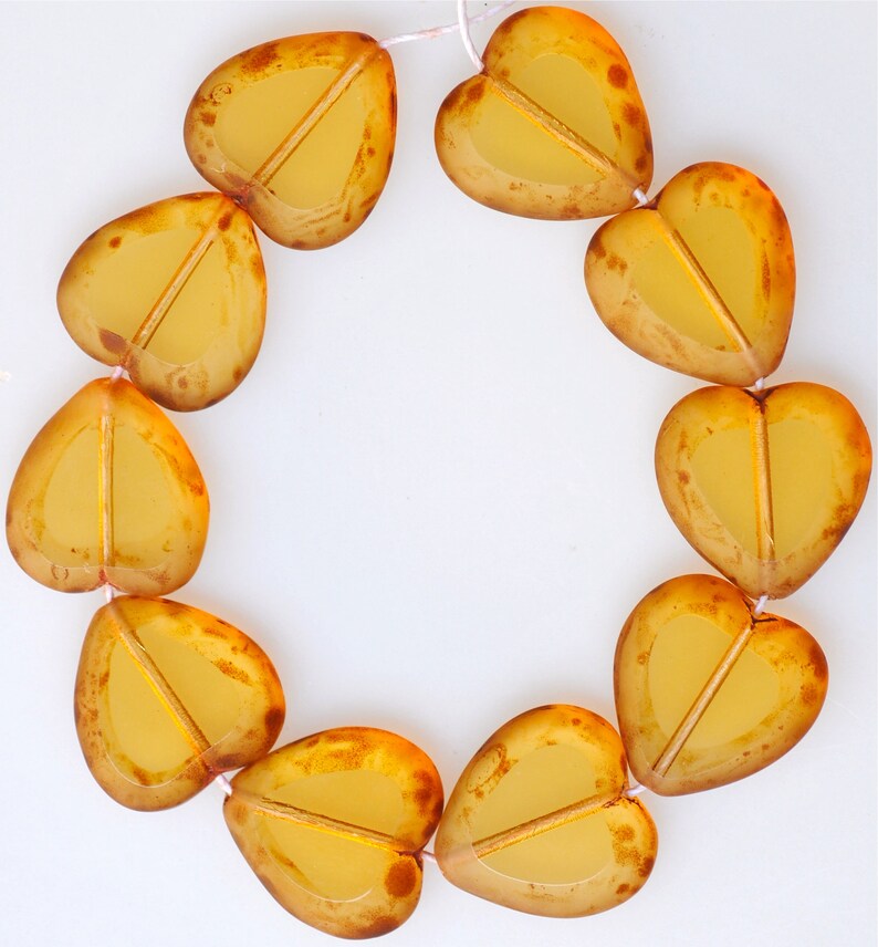 May include: A strand of amber-colored glass heart beads. The beads are strung together with a thin white thread. The beads are all heart-shaped and have a slightly translucent appearance.