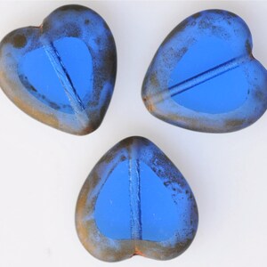 May include: Three blue glass heart-shaped beads with a distressed finish. The beads have a light blue center and a darker blue outer edge.