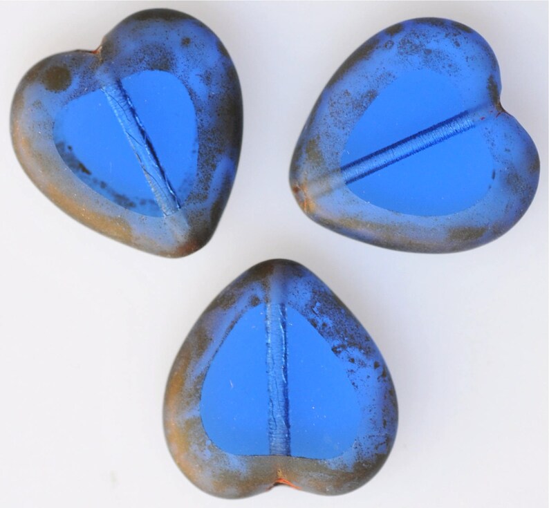 May include: Three blue glass heart-shaped beads with a distressed finish. The beads have a light blue center and a darker blue outer edge.