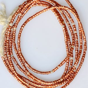 May include: A strand of copper-colored beads, strung on a white cord. The beads are small and round, with a slightly metallic sheen.