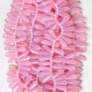 May include: Close-up of strands of pink teardrop-shaped beads. The beads are strung together, creating a delicate, floral-like pattern. The beads have a translucent quality, and the colour is a soft, pastel pink. The background is a plain white surface.
