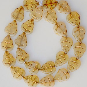 May include: A strand of glass beads in the shape of leaves. The beads are translucent and have a light amber color with gold leaf detailing.