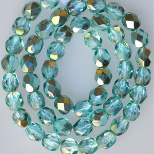 May include: A strand of turquoise blue glass beads with a faceted finish. The beads have a metallic sheen and are strung on a clear thread.