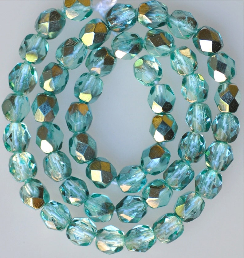 May include: A strand of turquoise blue glass beads with a faceted finish. The beads have a metallic sheen and are strung on a clear thread.