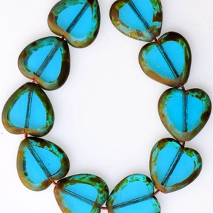May include: A strand of turquoise blue glass heart beads with a rustic brown finish. The beads are strung on a brown cord.