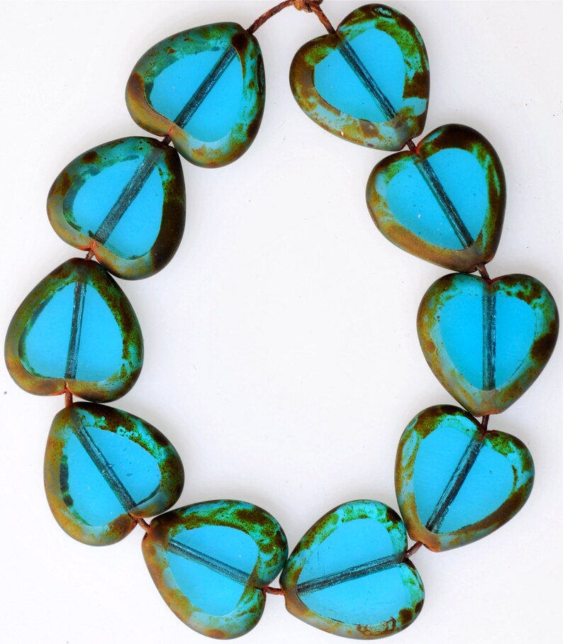 May include: A strand of turquoise blue glass heart beads with a rustic brown finish. The beads are strung on a brown cord.