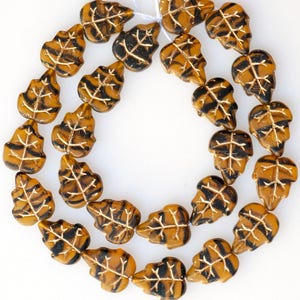 May include: A strand of brown and black glass beads in the shape of leaves. The beads have a metallic sheen and are strung on a white thread.