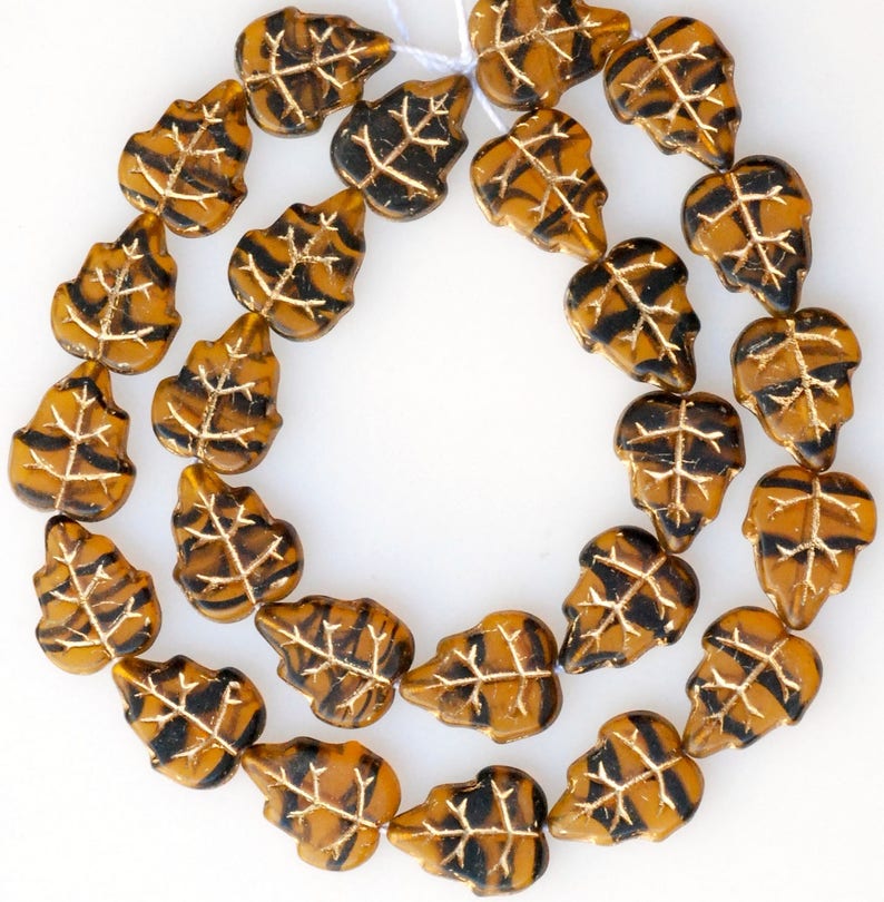 May include: A strand of brown and black glass beads in the shape of leaves. The beads have a metallic sheen and are strung on a white thread.
