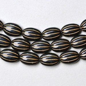 May include: A strand of black oval beads with gold stripes. The beads are strung together and are laying on a white surface.