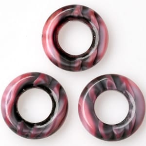 Op de afbeelding: Drie roze en zwarte plastic ringen met een spiraalpatroon en een gat in het midden.