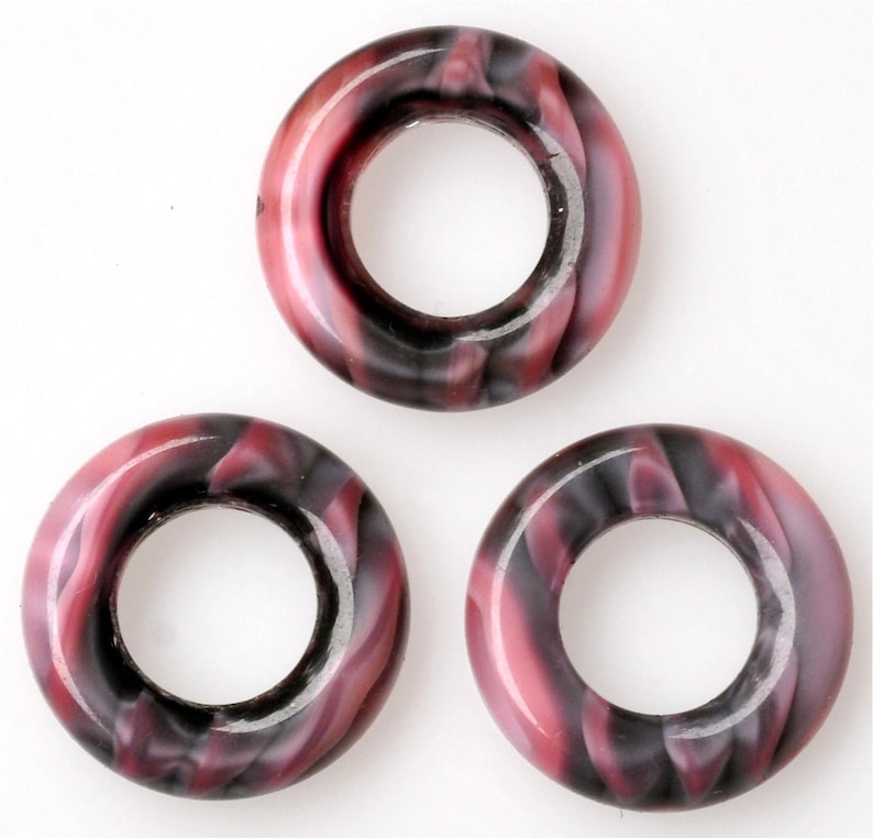 Puede incluir: Tres anillos de pl&aacute;stico de color rosa y negro con un patr&oacute;n de espiral y un agujero en el centro.