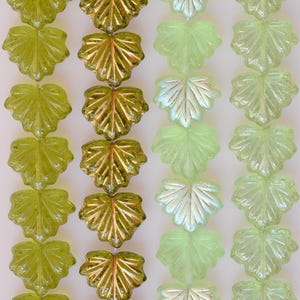 May include: Rows of glass leaf beads in shades of green and gold. The beads are shaped like leaves with detailed veining. The colors range from light green to a darker, golden hue. These beads are suitable for jewelry making and craft projects.